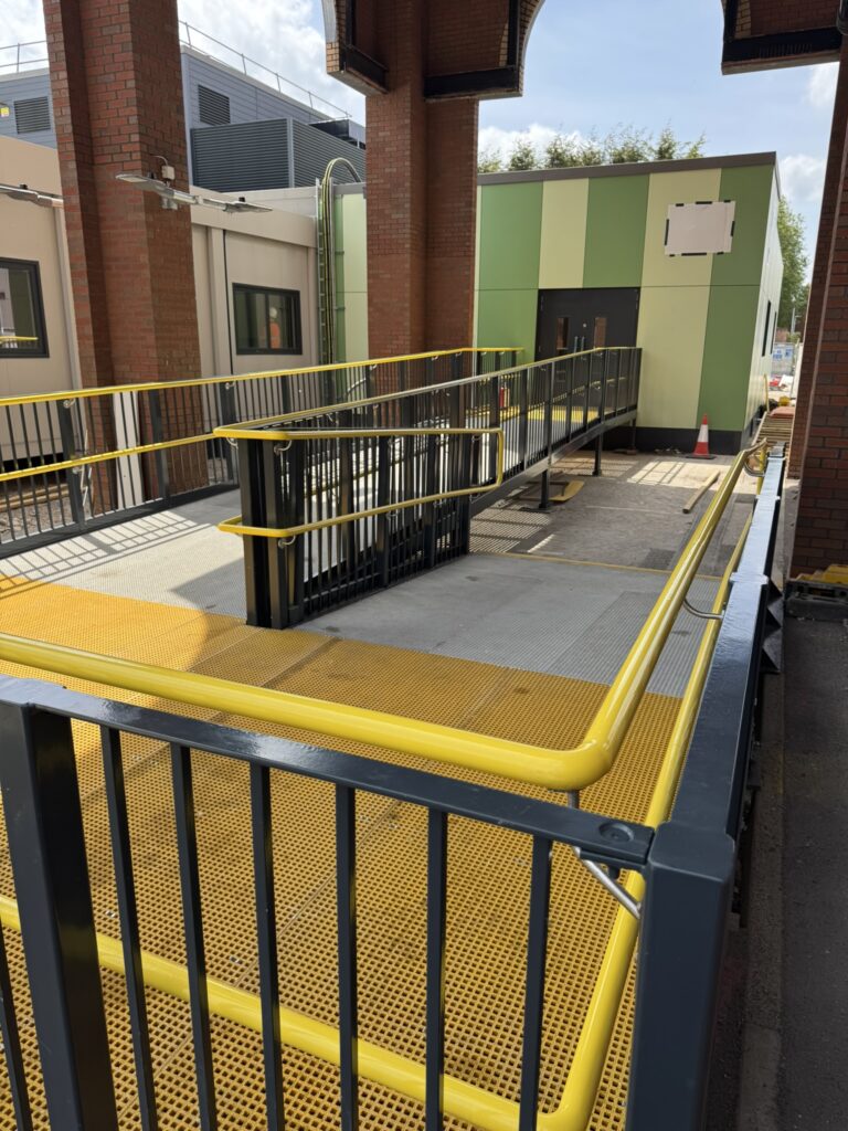 Bespoke steel access ramp with yellow handrails and non-slip GRP decking, designed and manufactured by Telford Fabrications.